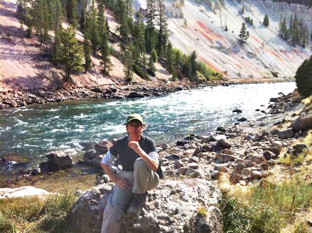 Laura standing on a rock at Yellowstone National Park next to a river and rocky slope